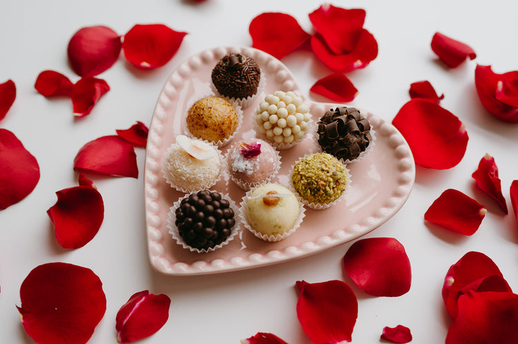 Assorted brigadeiros on a pink heart plate with rose petals